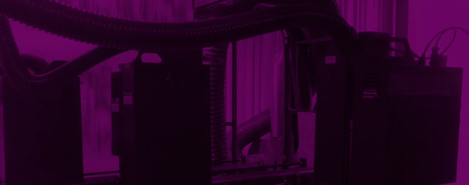 A close-up view of industrial machinery featuring tubing and electronic components against a vibrant purple backdrop.